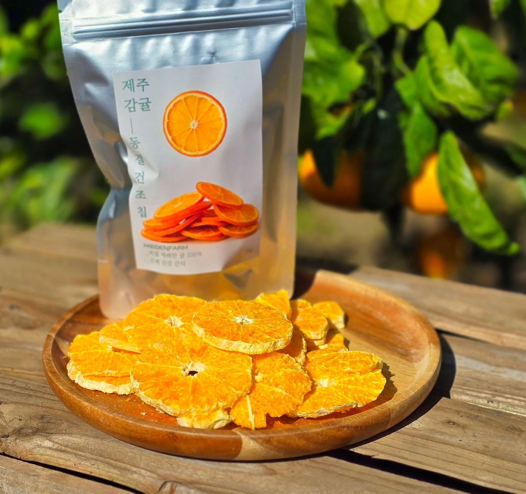 Tangerine chips on a wooden plate with a bag of Jeju tangerine freeze-dried chips (photo by MIEDEN FARM)